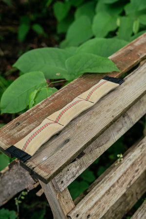 Squeaky snake dog toy made from upcycled firehose, resting on a wooden surface surrounded by greenery.