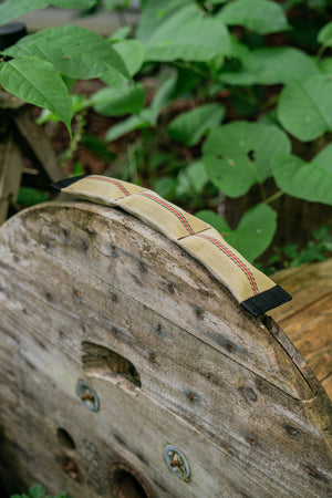 Upcycled firehose dog toy resting on a wooden spool amidst lush green foliage.