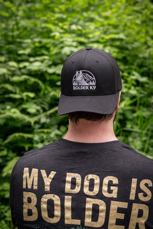 Man wearing Bolder K9 trucker hat in nature, showcasing adventure and outdoor lifestyle.