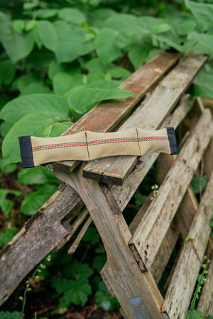Squeaky snake dog toy made from upcycled firehose, resting on a wooden pallet surrounded by greenery.