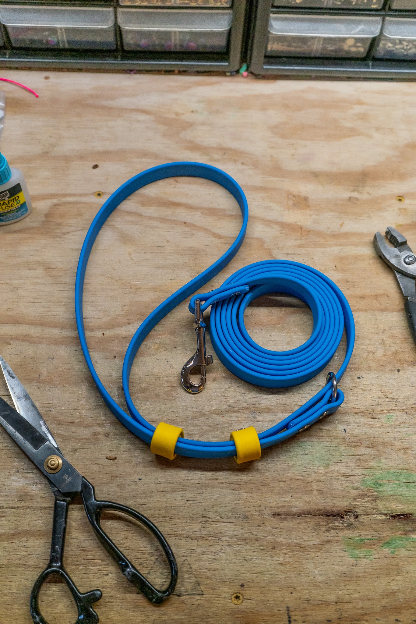 Hands-free adjustable bioThane leash in blue with yellow accents on a wooden table with scissors and tools.