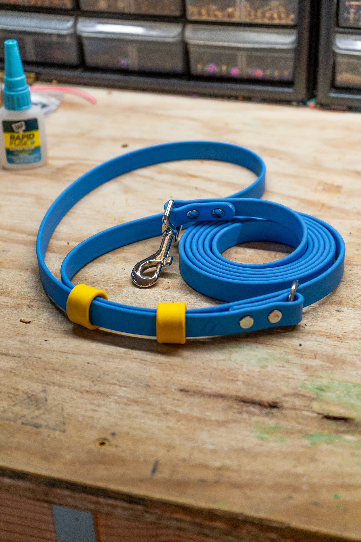 Eco adjustable length hands-free BioThane leash in blue with yellow accents on a wooden surface.